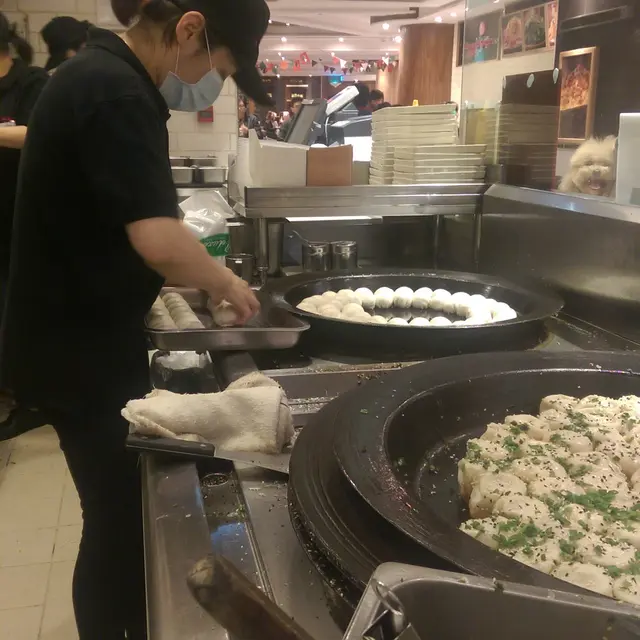 玻璃廚房內的員工包製生煎包,再將包好的放在生鐵平底鍋。